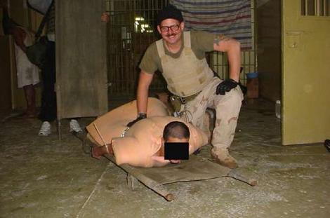 Charles Grainer smiles as he kneels over a helpless prisoner in newly released Abu Gharib photo